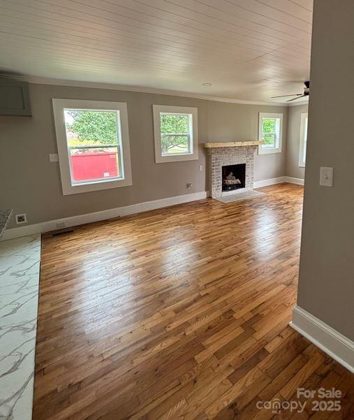 410 Gann St, Lowell, NC 28098 - unfurnished living room featuring wood finished floors, crown molding, a brick fireplace, baseboards, and ceiling fan