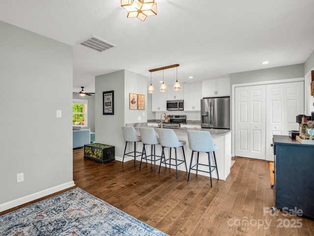 725 Center St, Asheville, NC 28803 - kitchen featuring stainless steel appliances, a peninsula, white cabinets, a kitchen bar, and wood finished floors