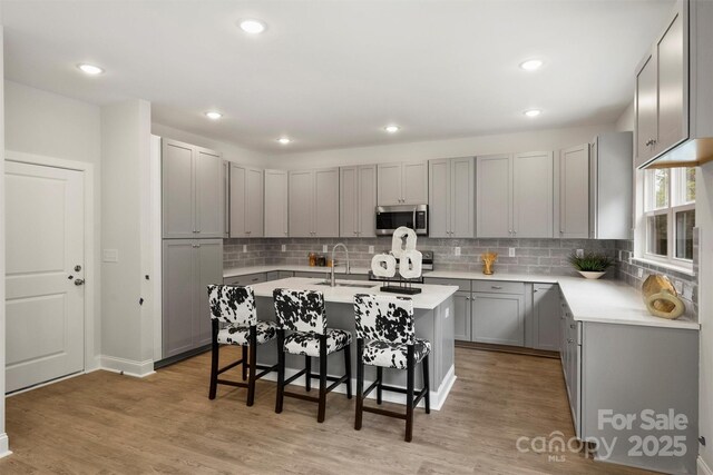 126 Meadow Glen Dr, Troutman, NC 28166 - kitchen featuring stainless steel microwave, gray cabinetry, a breakfast bar, a center island with sink, and stove
