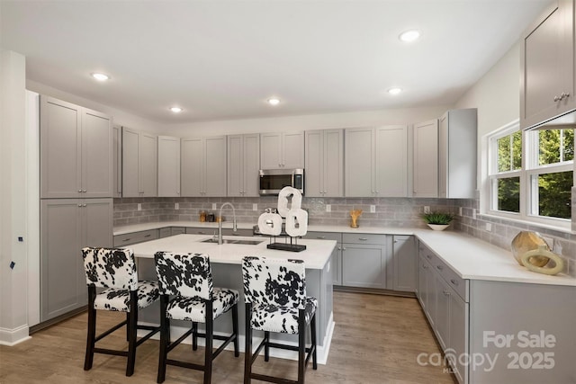 126 Meadow Glen Dr, Troutman, NC 28166 - kitchen with stainless steel microwave, a sink, gray cabinetry, a kitchen breakfast bar, and a center island with sink