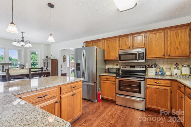 4527 Marshall Ct, Monroe, NC 28110 - kitchen featuring stainless steel appliances, brown cabinetry, pendant lighting, wood finished floors, and decorative backsplash