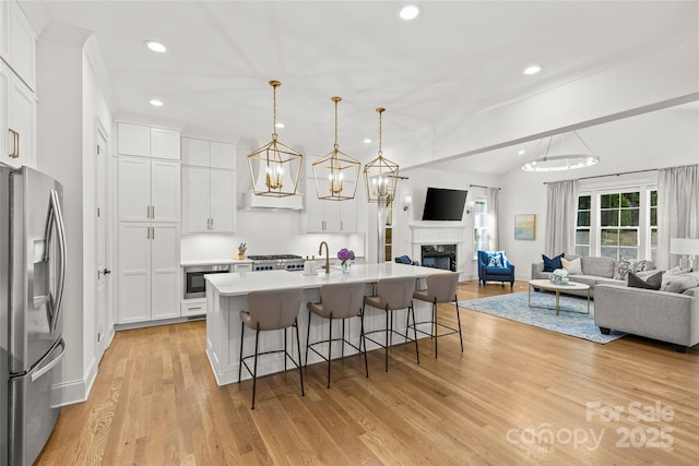 6013 Camile Ct, Charlotte, NC 28226 - kitchen featuring stainless steel fridge with ice dispenser, a kitchen bar, open floor plan, light wood finished floors, and a glass covered fireplace