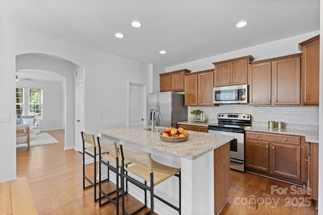 10027 Juniper Trace Dr, Charlotte, NC 28277 - kitchen featuring stainless steel appliances, arched walkways, an island with sink, tasteful backsplash, and dark wood-style flooring
