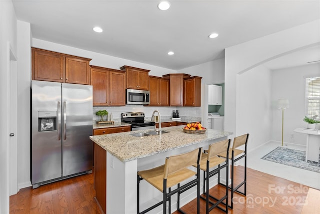 10027 Juniper Trace Dr, Charlotte, NC 28277 - kitchen featuring appliances with stainless steel finishes, independent washer and dryer, tasteful backsplash, light stone counters, and a center island with sink