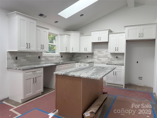 2027 Marquesas Ave, Tega Cay, SC 29708 - kitchen with vaulted ceiling, a skylight, white cabinetry, tasteful backsplash, and light stone counters