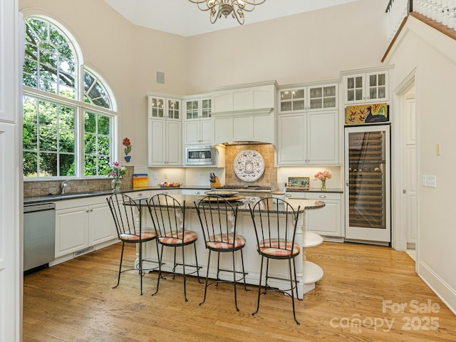 2516 Selwyn Ave, Charlotte, NC 28209 - kitchen featuring beverage cooler, stainless steel appliances, light wood finished floors, decorative backsplash, and a high ceiling
