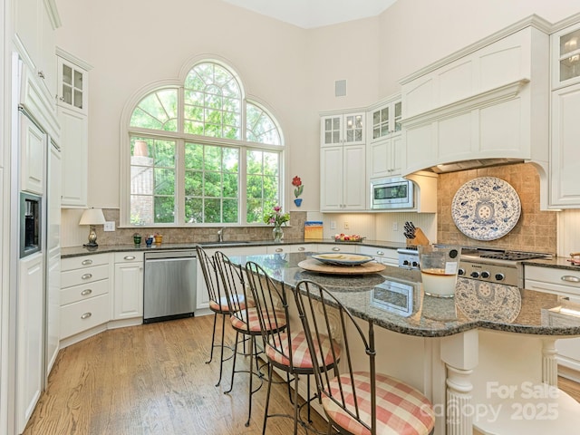 2516 Selwyn Ave, Charlotte, NC 28209 - kitchen featuring appliances with stainless steel finishes, a towering ceiling, a sink, light wood-type flooring, and a kitchen breakfast bar