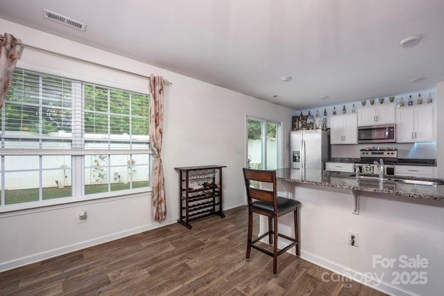 7527 Finnigan Rd, Charlotte, NC 28215 - kitchen featuring stainless steel appliances, a kitchen breakfast bar, dark wood-style flooring, white cabinetry, and dark stone counters