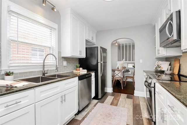 2421 Shamrock Dr, Charlotte, NC 28205 - kitchen featuring stainless steel appliances, a sink, arched walkways, light wood-style floors, and white cabinetry