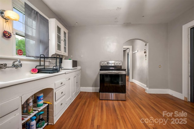 123 N Poston St, Shelby, NC 28150 - kitchen with stainless steel range with electric stovetop, white microwave, arched walkways, white cabinetry, and wood finished floors