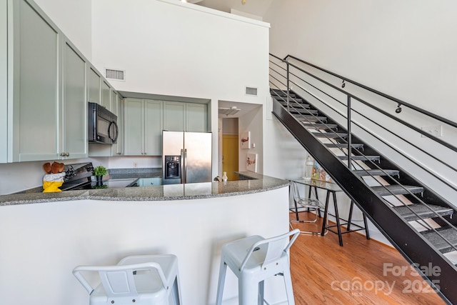 115 E Park Ave Unit 409, Charlotte, NC 28203 - kitchen featuring black appliances, light wood-type flooring, a peninsula, a towering ceiling, and a breakfast bar