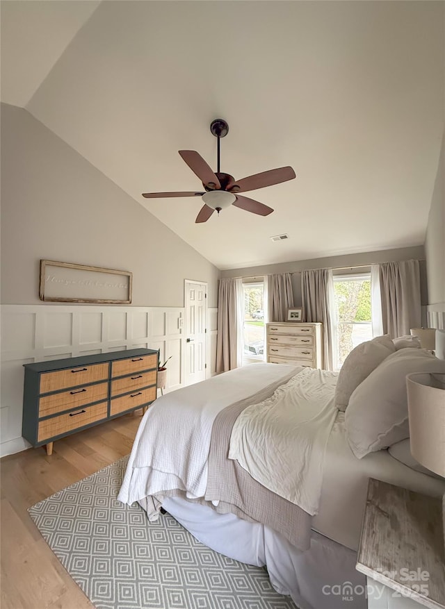 3314 Mara Ct, Matthews, NC 28105 - bedroom featuring vaulted ceiling, light wood-type flooring, a ceiling fan, a wainscoted wall, and a decorative wall