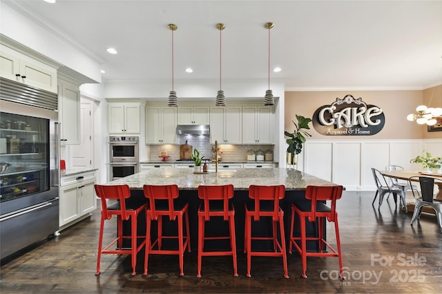 164 Twin Sisters Ln, Mooresville, NC 28117 - kitchen with appliances with stainless steel finishes, under cabinet range hood, crown molding, a kitchen island with sink, and decorative backsplash