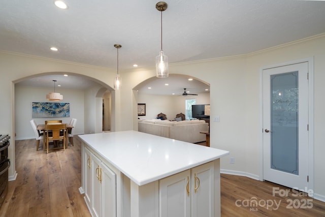 16132 Mclester Rd, Oakboro, NC 28129 - kitchen with arched walkways, a ceiling fan, a kitchen island, wood finished floors, and ornamental molding