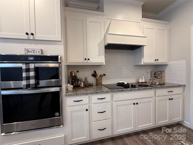 1016 Laggan Ln, Indian Trail, NC 28079 - kitchen with custom range hood, black electric stovetop, stainless steel double oven, ornamental molding, and white cabinets