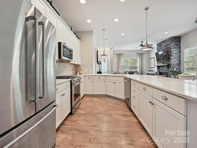 9405 Gladden Hill Ln, Pineville, NC 28134 - kitchen featuring high end appliances, a stone fireplace, light wood-style flooring, ceiling fan, and light countertops