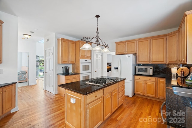 11917 Ulsten Ln, Huntersville, NC 28078 - kitchen featuring appliances with stainless steel finishes, light wood-style flooring, a kitchen island, tasteful backsplash, and dark stone countertops