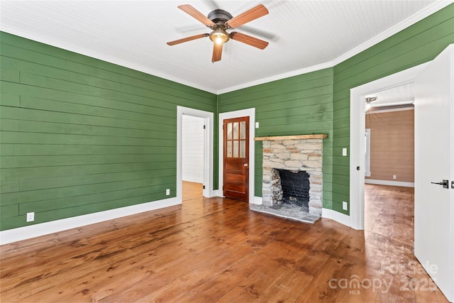 233 Sellars Rd, Kings Mountain, NC 28086 - unfurnished living room featuring ceiling fan, ornamental molding, a stone fireplace, hardwood / wood-style floors, and wooden walls