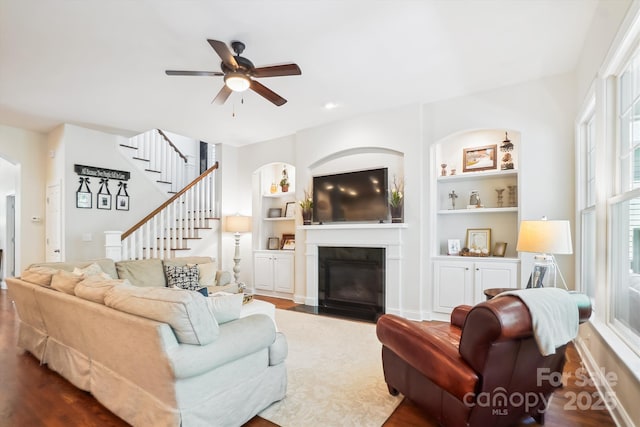 5424 Morris Hunt Dr, Fort Mill, SC 29708 - living room featuring a fireplace with flush hearth, a ceiling fan, built in features, dark wood finished floors, and stairs