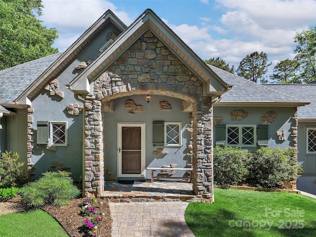 92 Island View Ct, Mill Spring, NC 28756 - view of exterior entry with stone siding, a shingled roof, stucco siding, and covered porch