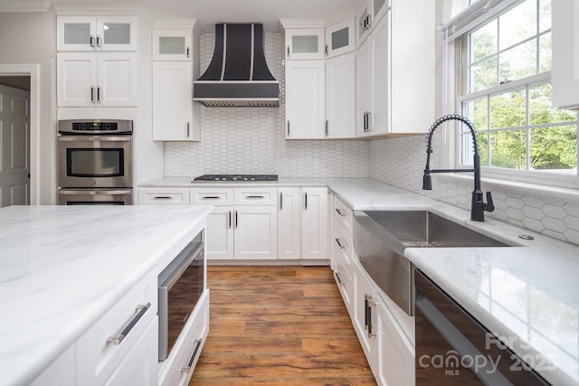 6400 Morningsong Ln, Charlotte, NC 28269 - kitchen featuring custom exhaust hood, stainless steel appliances, white cabinets, light wood-style floors, and light stone countertops