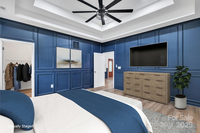 1246 Bob Falls Rd, Shelby, NC 28150 - bedroom featuring a tray ceiling, a decorative wall, light wood-style floors, a walk in closet, and a ceiling fan