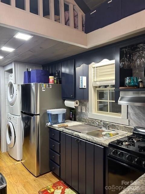623 Overlook Dr, Spruce Pine, NC 28777 - kitchen with black gas range, stacked washer / dryer, wall chimney exhaust hood, light wood-style floors, and freestanding refrigerator