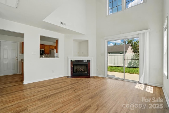 8605 Sawleaf Ct, Charlotte, NC 28215 - unfurnished living room featuring a high ceiling, light wood-style floors, plenty of natural light, baseboards, and a fireplace