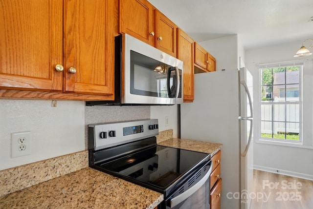8605 Sawleaf Ct, Charlotte, NC 28215 - kitchen with stainless steel appliances, brown cabinets, light wood-style floors, light stone counters, and tasteful backsplash