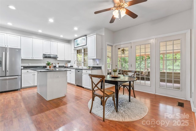 5233 Fairvista Dr, Charlotte, NC 28269 - kitchen with stainless steel appliances, under cabinet range hood, a center island, white cabinets, and dark countertops