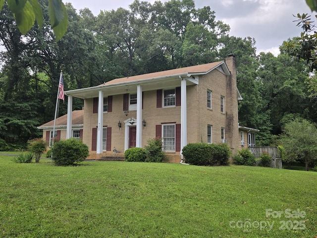 9225 Robinson Church Rd, Charlotte, NC 28215 - neoclassical home featuring a front yard, brick siding, a chimney, and view of wooded area