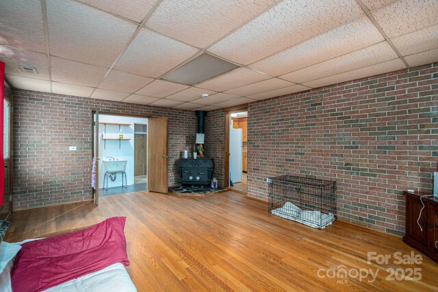 3120 7th Street Dr NE, Hickory, NC 28601 - living area featuring a paneled ceiling, a wood stove, brick wall, and wood finished floors
