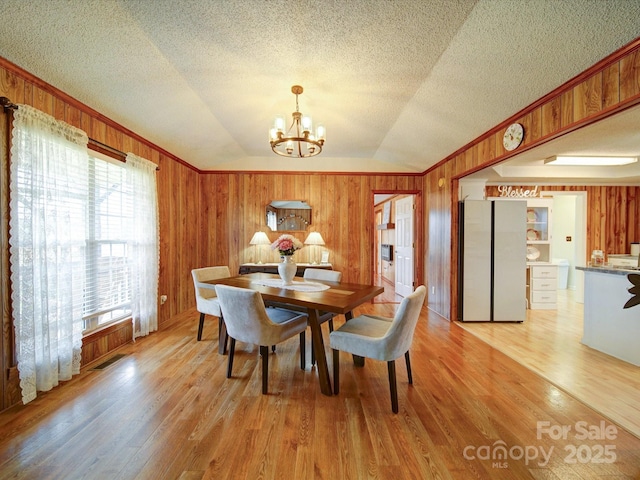 4115 Jenkins Rd, Marshville, NC 28103 - dining room featuring a chandelier, wood walls, light wood-style floors, a textured ceiling, and vaulted ceiling