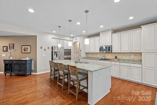 7339 Millstone Cir SW, Concord, NC 28025 - kitchen featuring appliances with stainless steel finishes, a sink, a breakfast bar area, light wood-style flooring, and a center island with sink