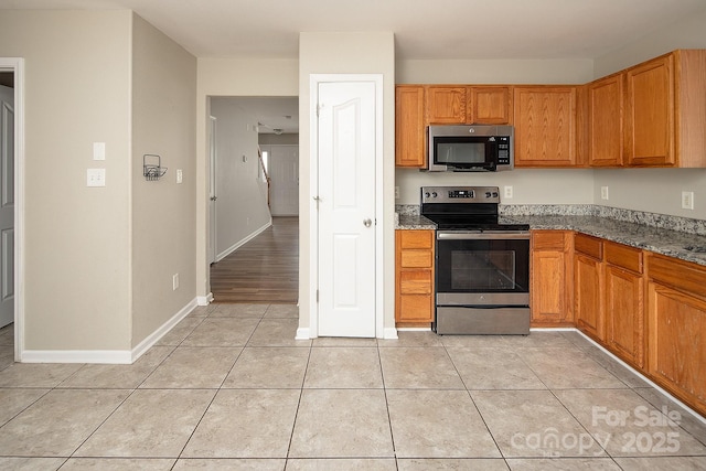 8432 Spirea Ct, Charlotte, NC 28215 - kitchen with stainless steel appliances, light tile patterned floors, dark stone counters, baseboards, and brown cabinets