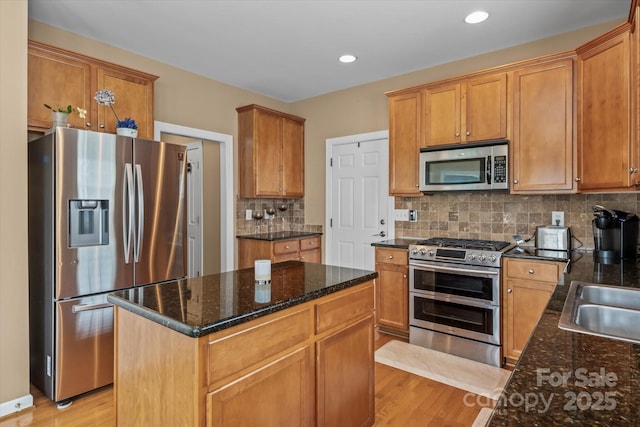 108 Planters Dr, Statesville, NC 28677 - kitchen featuring appliances with stainless steel finishes, light wood-style floors, decorative backsplash, dark stone countertops, and a kitchen island