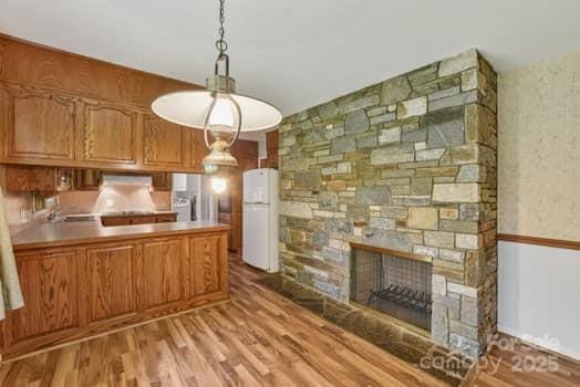 125 Merrill Rd, Fletcher, NC 28732 - kitchen with freestanding refrigerator, light wood-type flooring, a peninsula, a stone fireplace, and brown cabinets