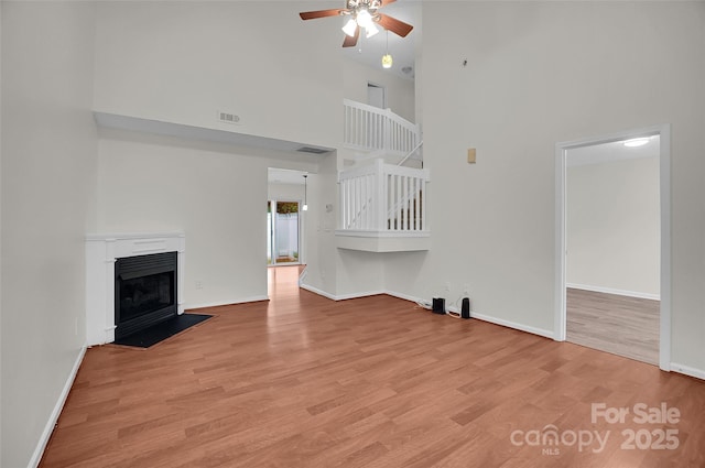 5237 Ficus Tree Ln, Charlotte, NC 28215 - unfurnished living room featuring a towering ceiling, a ceiling fan, light wood finished floors, and a fireplace with flush hearth