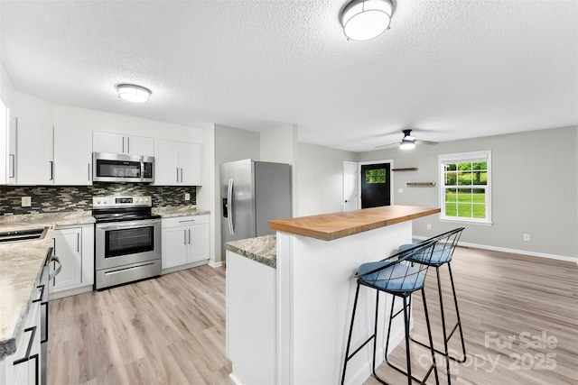 103A N Tracy St, Kings Mountain, NC 28086 - kitchen with appliances with stainless steel finishes, wood counters, a textured ceiling, a kitchen breakfast bar, and light wood finished floors