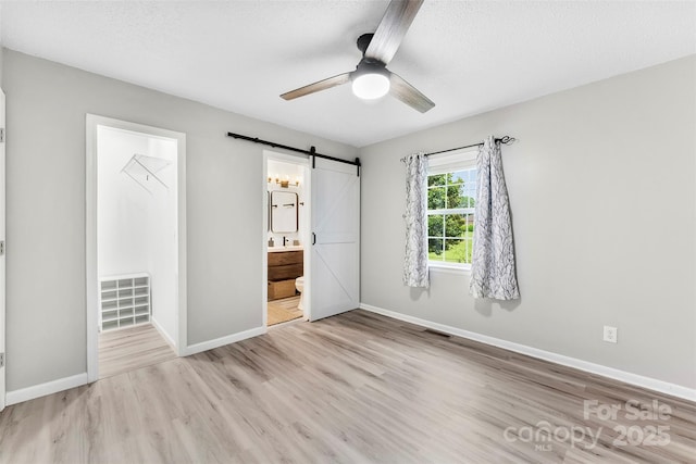 103A N Tracy St, Kings Mountain, NC 28086 - unfurnished bedroom with a barn door, light wood finished floors, baseboards, ensuite bath, and a textured ceiling