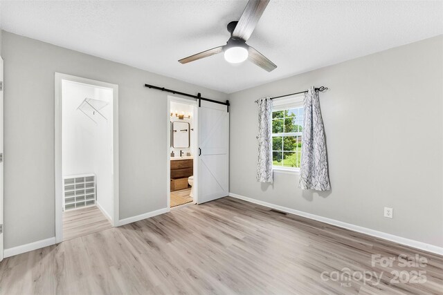 103A N Tracy St, Kings Mountain, NC 28086 - unfurnished bedroom featuring a barn door, light wood-style floors, ensuite bath, ceiling fan, and a textured ceiling