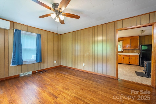 1788 Blue Rock Rd, Burnsville, NC 28714 - unfurnished living room featuring a wood stove, light wood finished floors, a ceiling fan, wooden walls, and baseboards