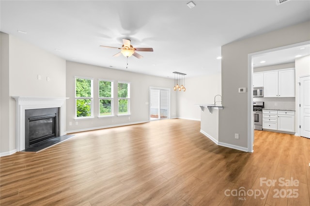4848 Fonthill Ln, Charlotte, NC 28210 - unfurnished living room with a ceiling fan, a glass covered fireplace, light wood finished floors, a sink, and baseboards