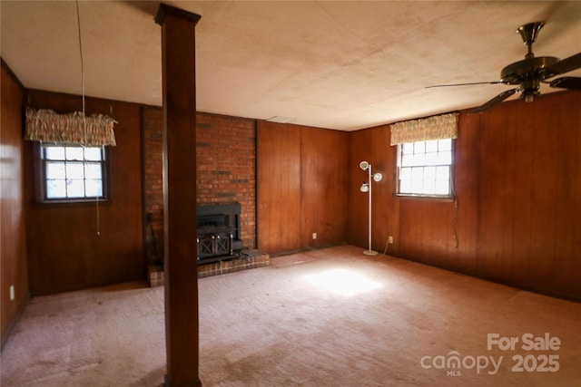 170 Heritage Ln, Salisbury, NC 28147 - unfurnished living room featuring a wood stove, carpet floors, wooden walls, and a ceiling fan