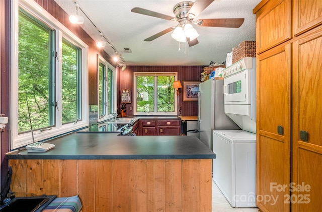 1102 Lake Montonia Rd, Kings Mountain, NC 28086 - kitchen with stacked washer and clothes dryer, track lighting, a ceiling fan, dark countertops, and a peninsula