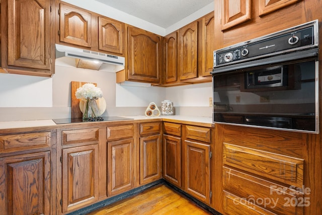220 W Park Dr, Morganton, NC 28655 - kitchen with under cabinet range hood, black appliances, brown cabinetry, and light wood-style flooring