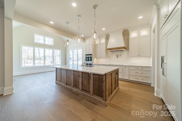 608 Deodar Cedar Dr Unit 69, Matthews, NC 28104 - kitchen with custom exhaust hood, oven, light countertops, light wood-style floors, and glass insert cabinets
