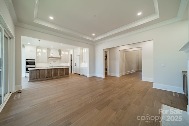 608 Deodar Cedar Dr Unit 69, Matthews, NC 28104 - unfurnished living room featuring a tray ceiling, a sink, ornamental molding, recessed lighting, and light wood-style flooring