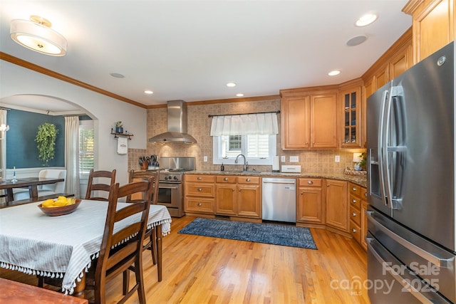 141 Eastover Dr SE, Concord, NC 28025 - kitchen featuring appliances with stainless steel finishes, wall chimney range hood, light wood finished floors, arched walkways, and crown molding