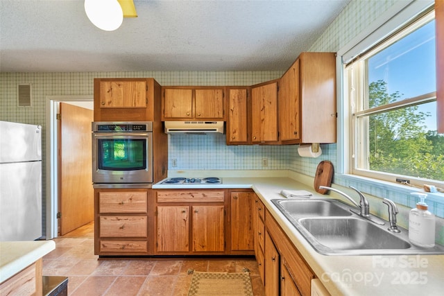 55 Dane Acres Dr, Alexander, NC 28701 - kitchen featuring appliances with stainless steel finishes, under cabinet range hood, wallpapered walls, light countertops, and brown cabinetry